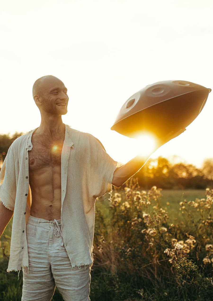 Malte Marten holding a handpan against the setting sun in an open field