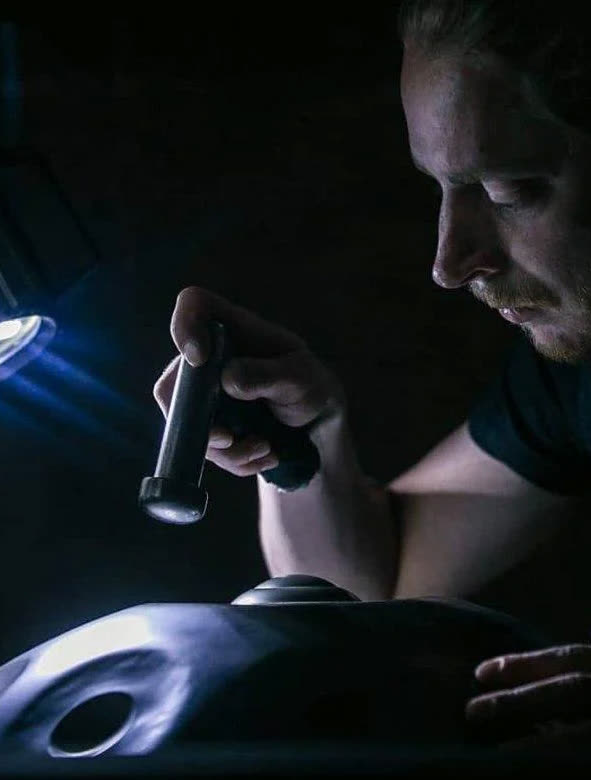 Ralf van den Bor inspecting a handpan shell by torchlight in the workshop